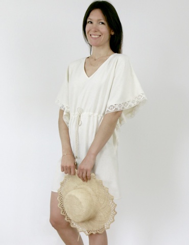 Robe Helios version courte et grandes manches, en soie blanc cassé avec galon de dentelle, chapeau de paille à la main